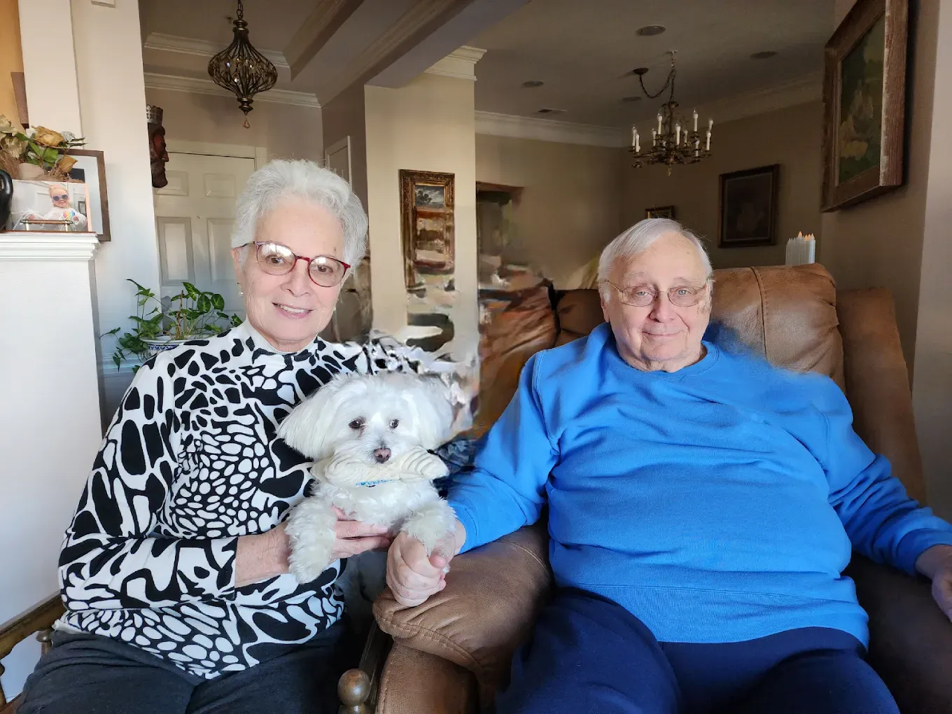 A man and a woman are sitting in a chair holding a small white dog.