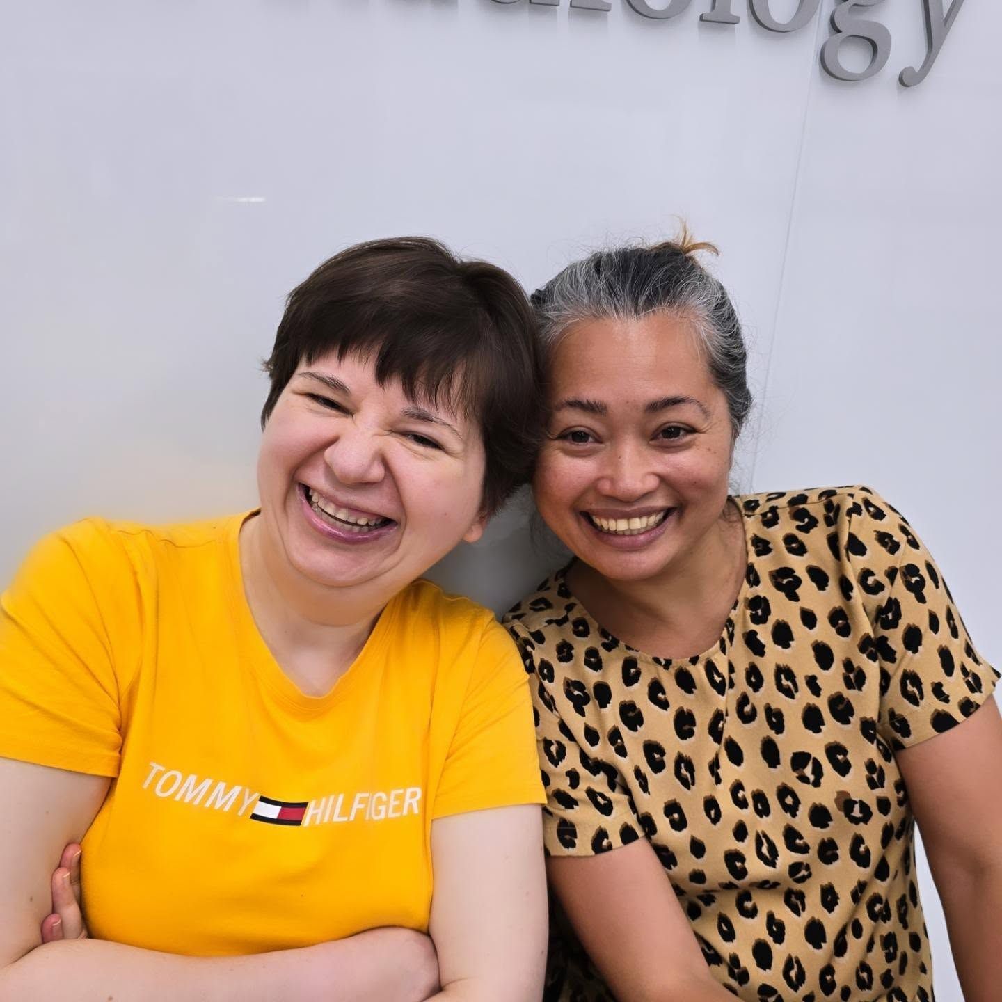 Two women are posing for a picture and one is wearing a yellow tommy hilfiger shirt