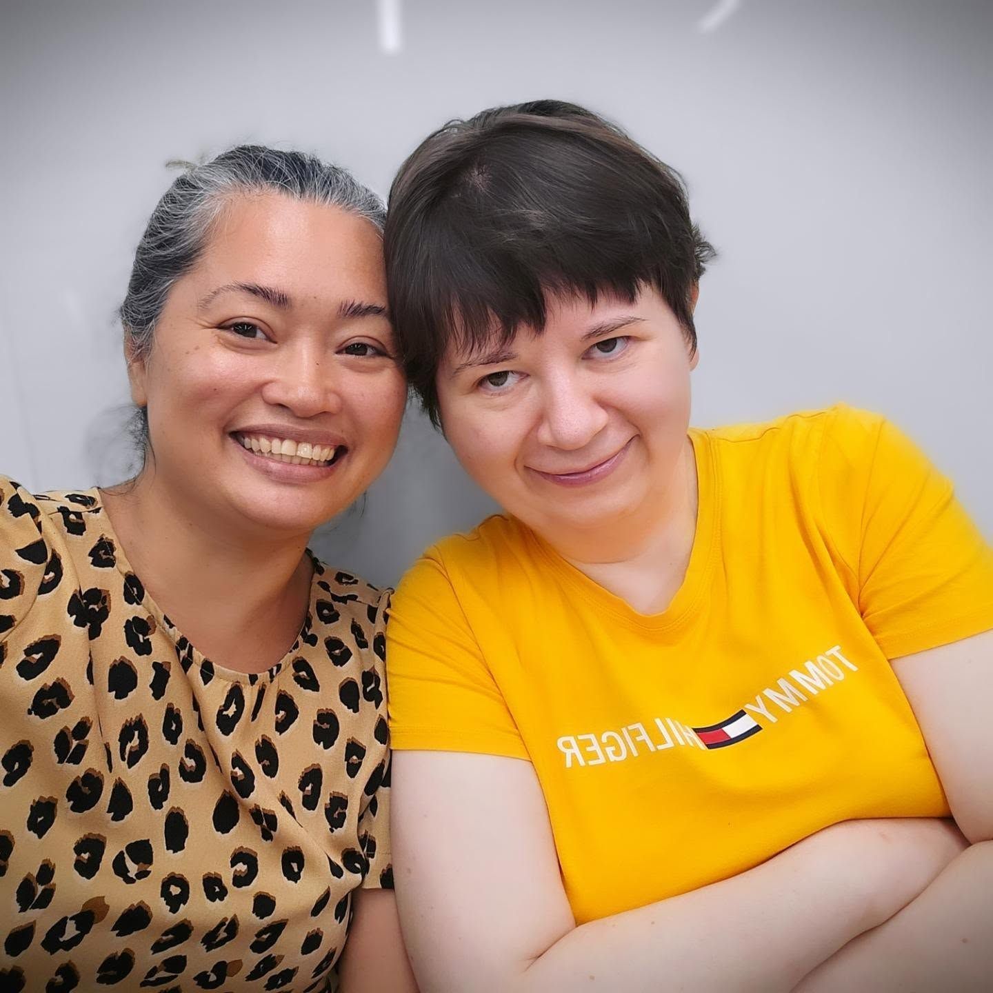Two women are posing for a picture and one is wearing a yellow shirt that says tommy hilfiger