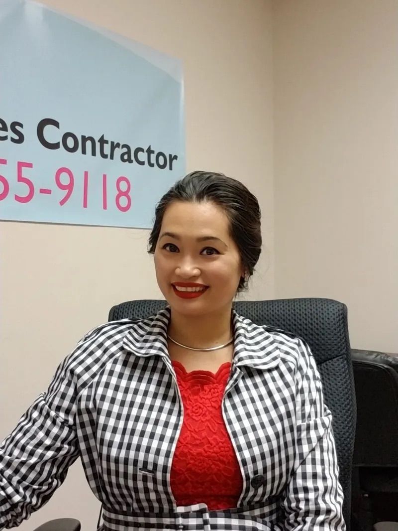 A woman sitting in front of a sign that says contractor 55-9118
