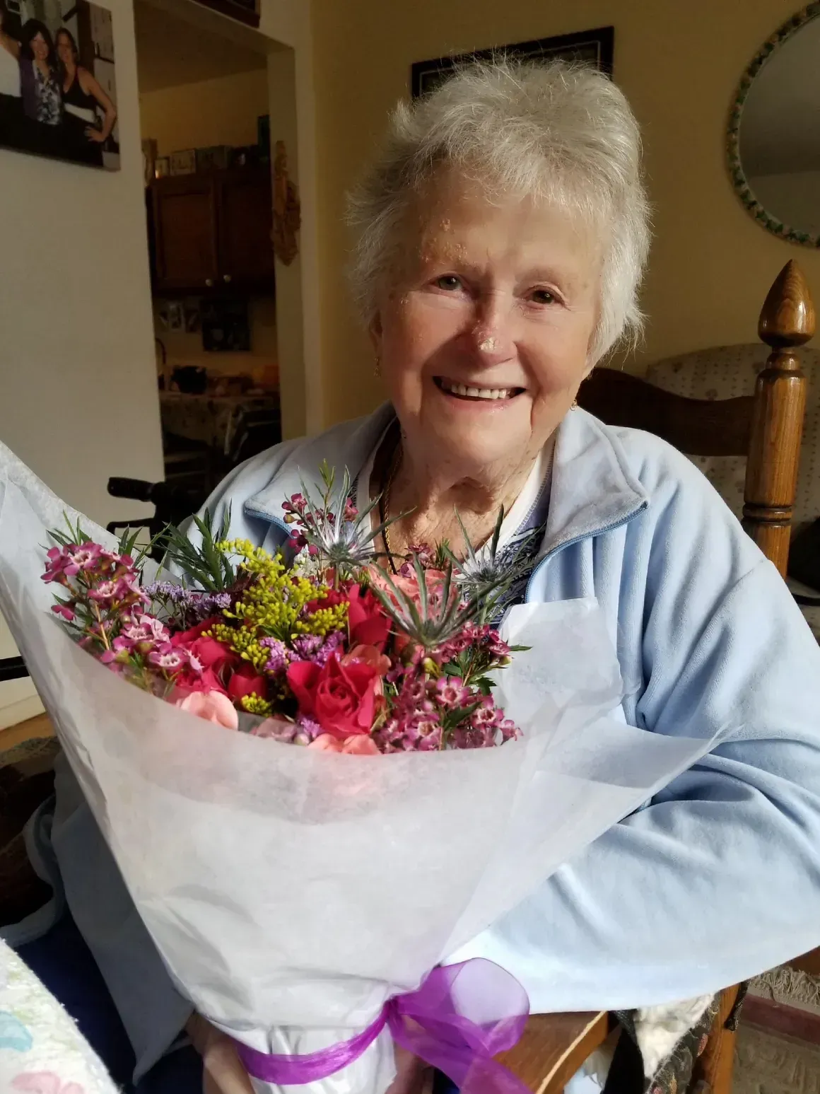 An elderly woman is holding a bouquet of flowers and smiling.