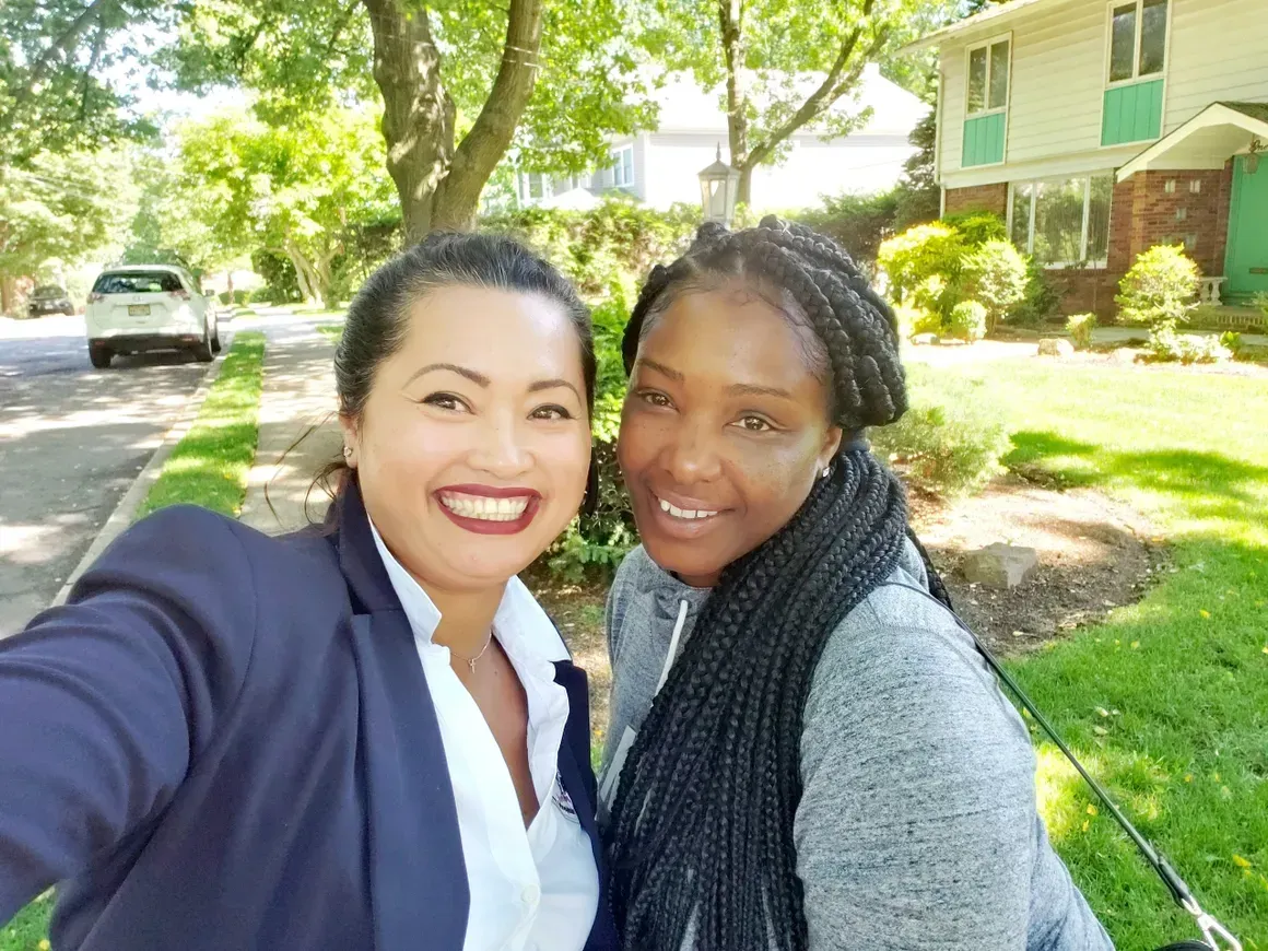 Two women are posing for a selfie in front of a house.