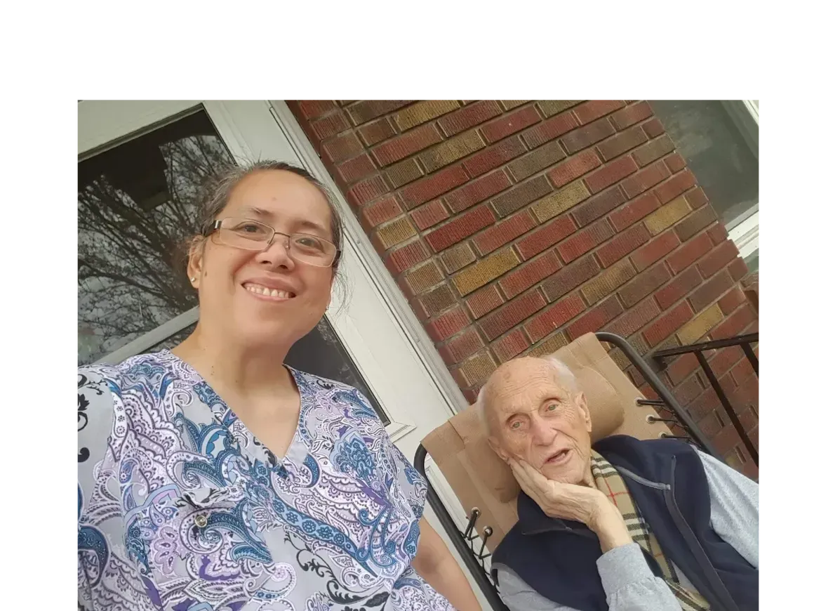 A woman is sitting next to an elderly man in a chair on a porch.