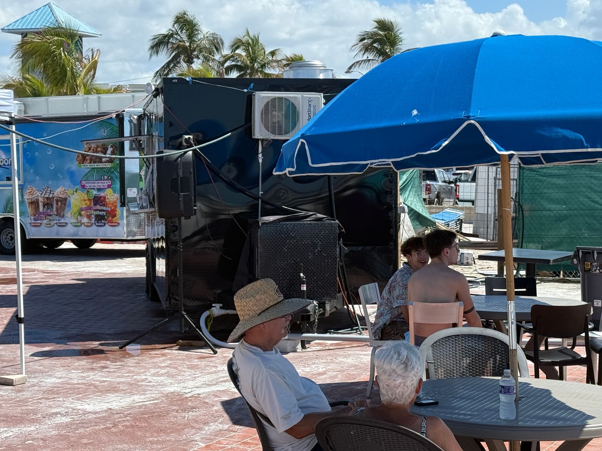 People sitting at outdoor tables, near food trucks on a sunny day.