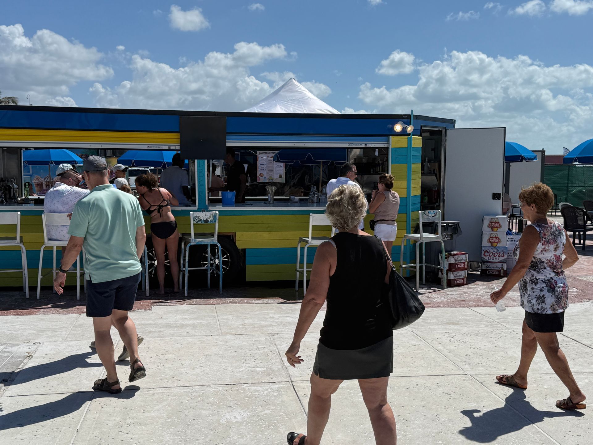 People walking near a brightly painted bar on a sunny day.
