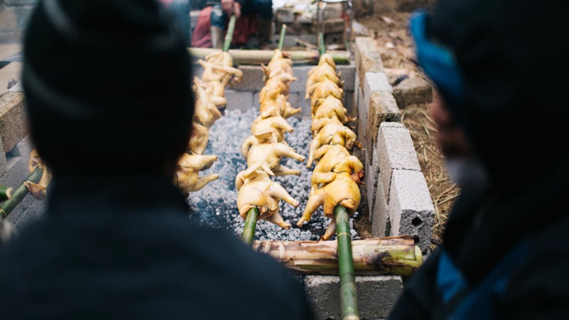 Un grupo de personas está cocinando pollos en una parrilla.