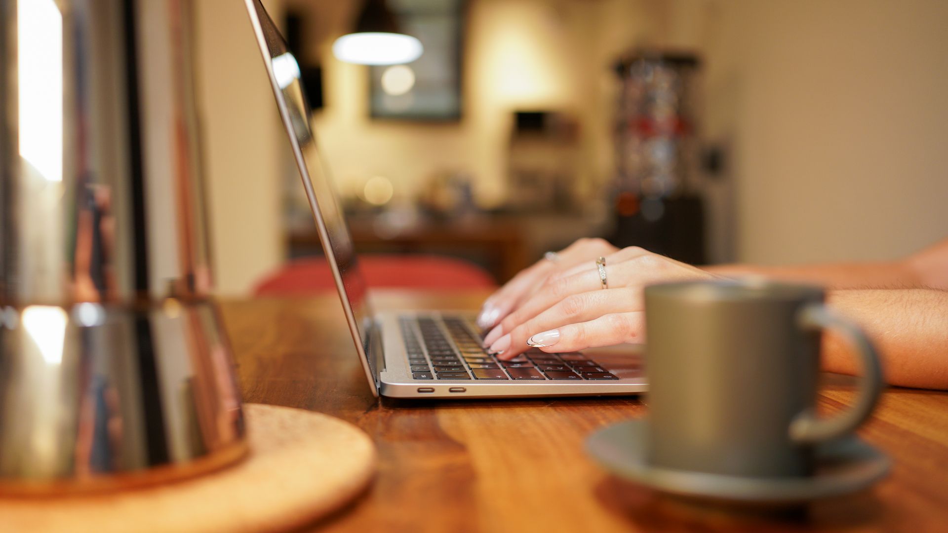 Persona che scrive su un computer portatile con una tazza di caffè e una caffettiera su un tavolo di legno.