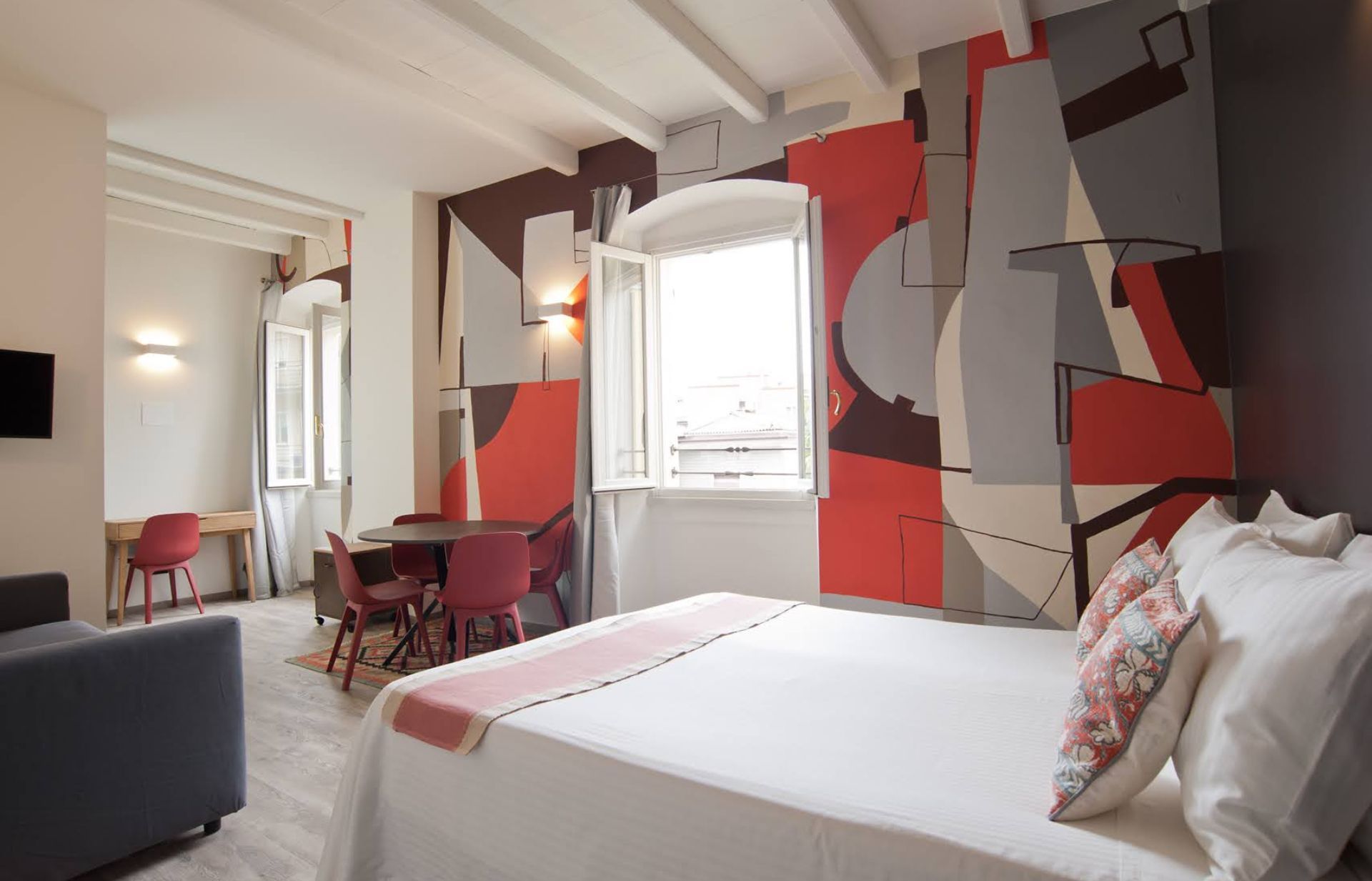 Camera da letto con parete murale astratta, letto, tavolo da pranzo e finestra aperta.