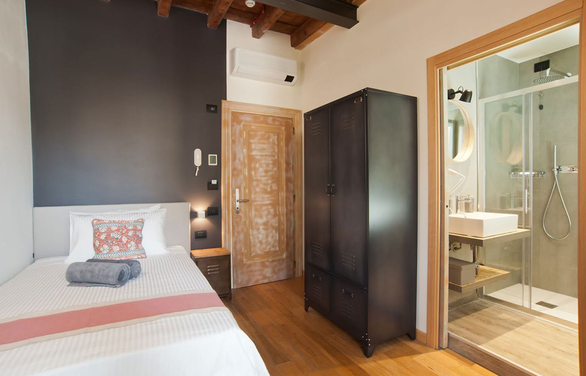 Camera da letto con letto, armadio e bagno. Parete decorativa grigio scuro, pavimenti in legno chiaro.