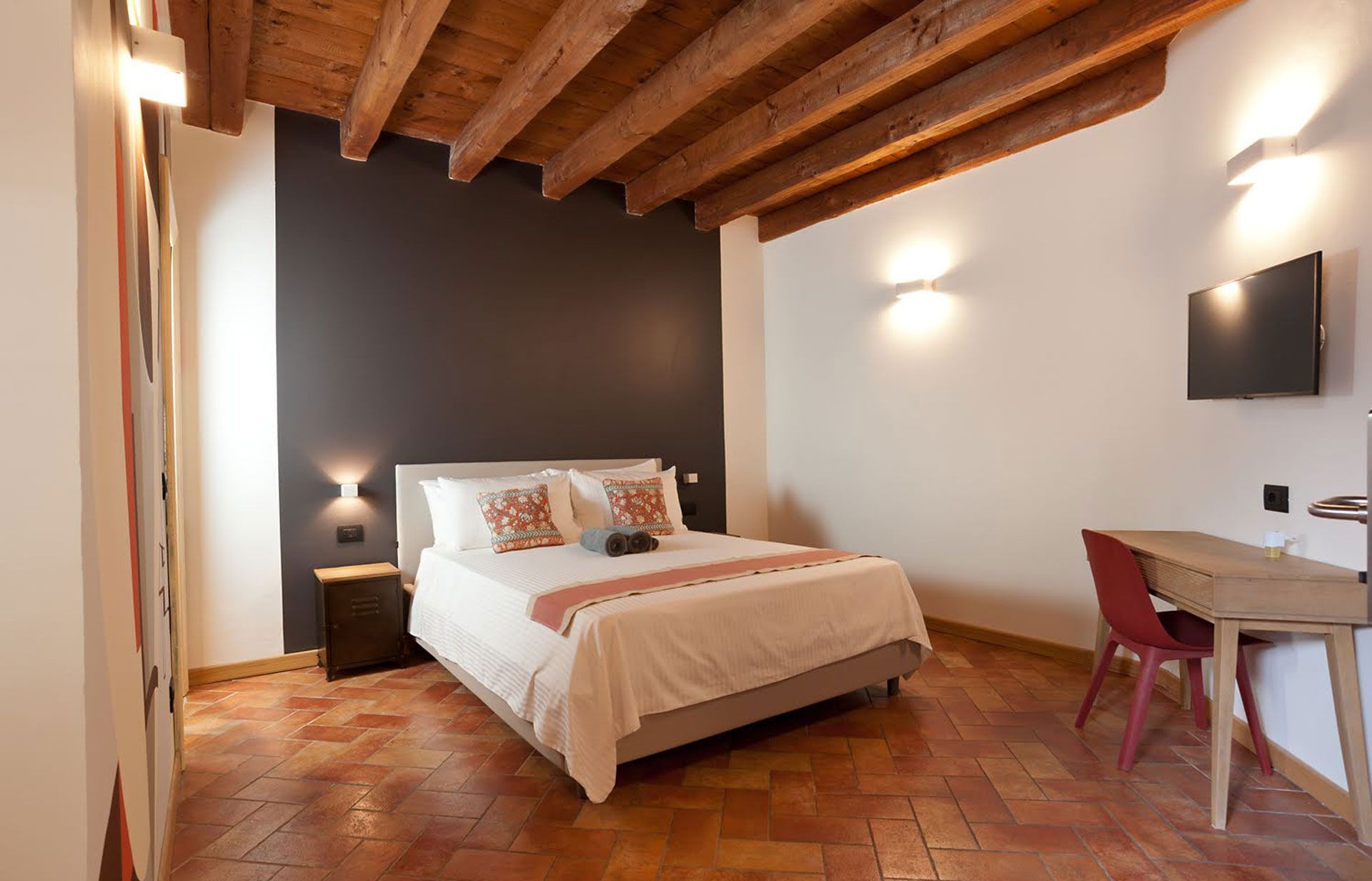 Camera da letto con letto, travi in ​​legno, parete con accenti scuri e scrivania.