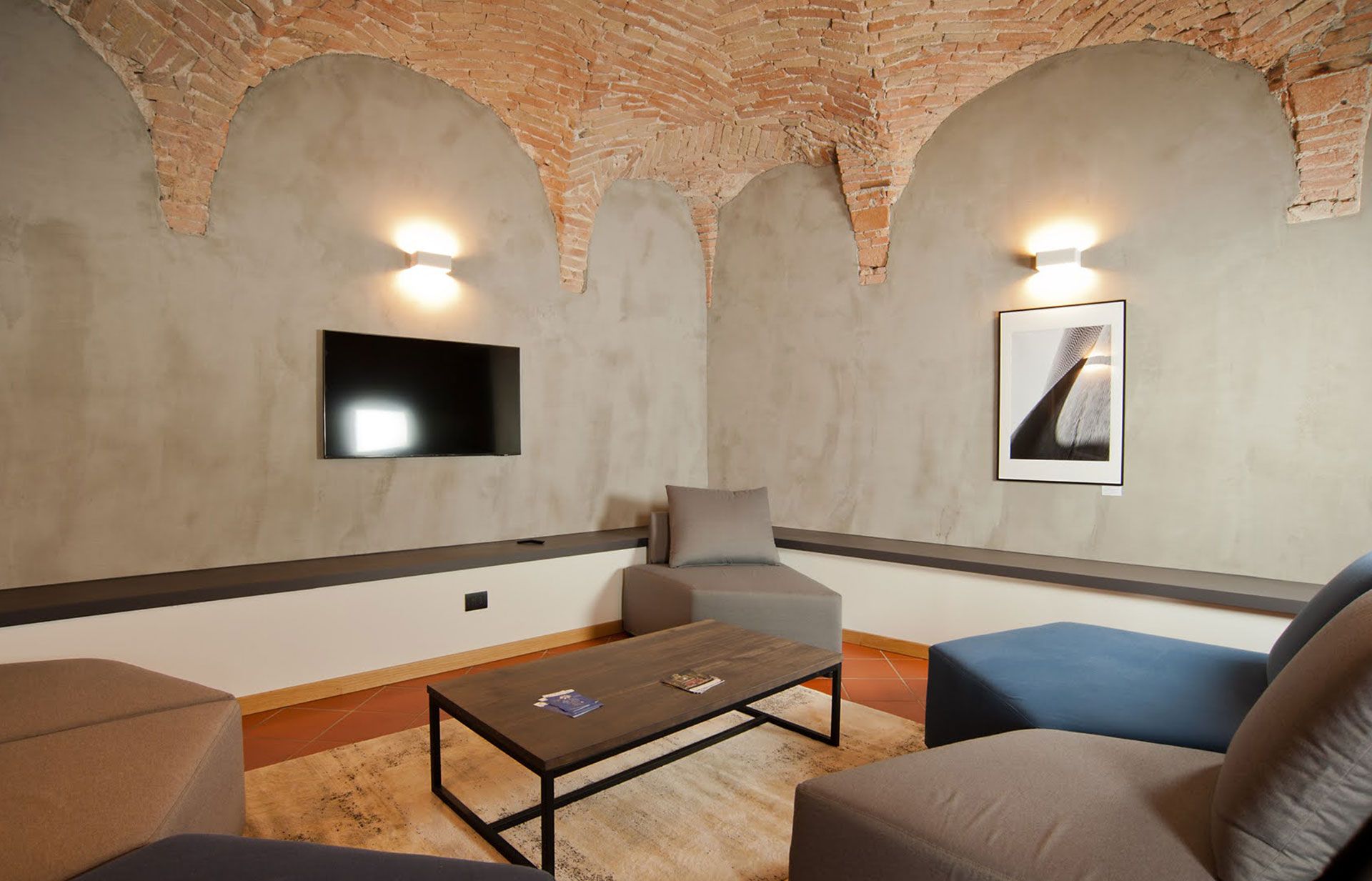 Accogliente soggiorno con pareti grigie, archi in mattoni sul soffitto, TV, posti a sedere e un moderno tavolino da caffè.