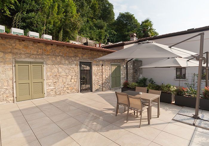 Patio esterno con tavolo e sedie, ombreggiato da un grande ombrellone, addossato a un edificio in pietra.