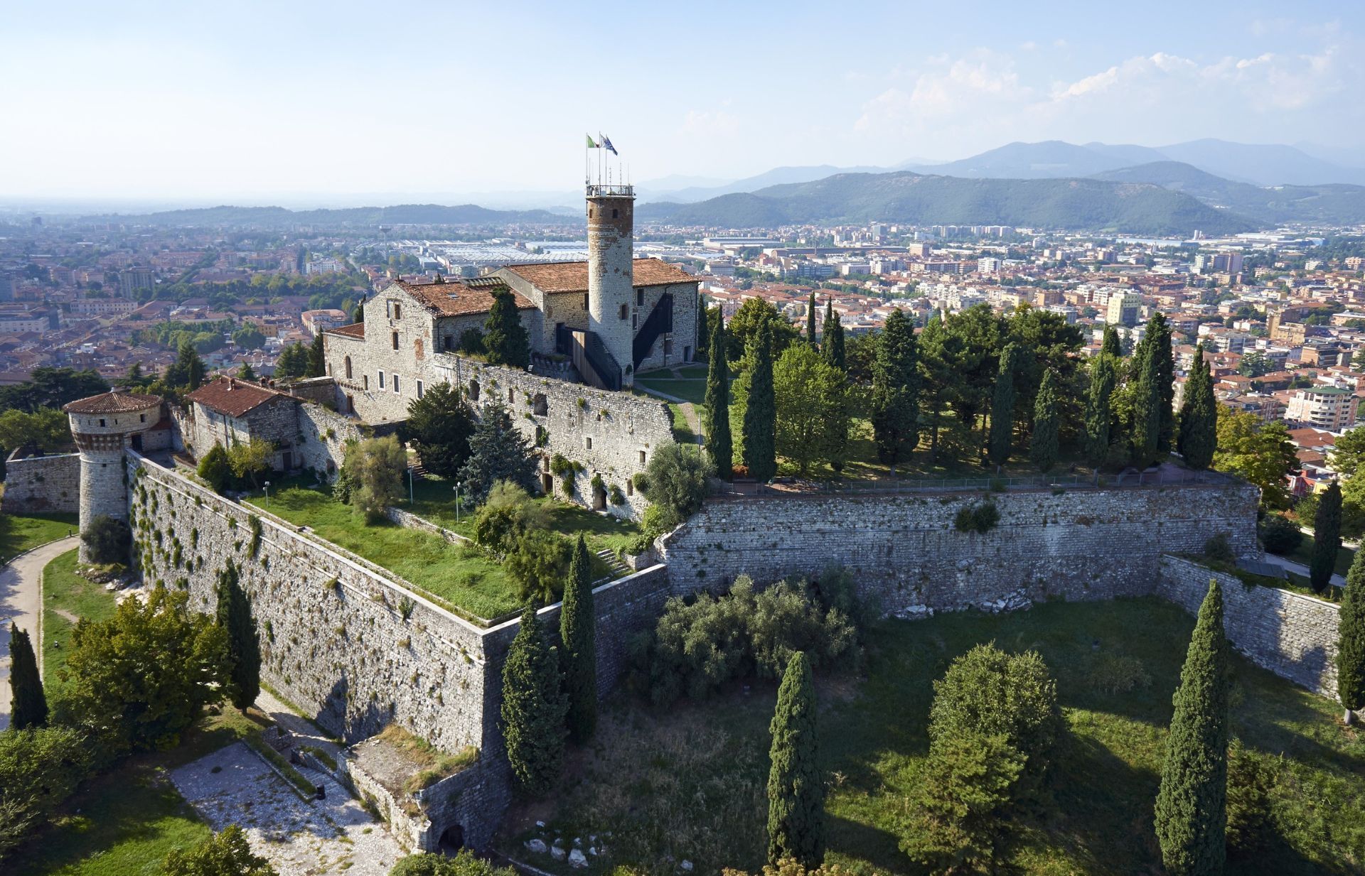 Un castello di pietra si erge in cima a una collina, dominando una città con le montagne sullo sfondo.