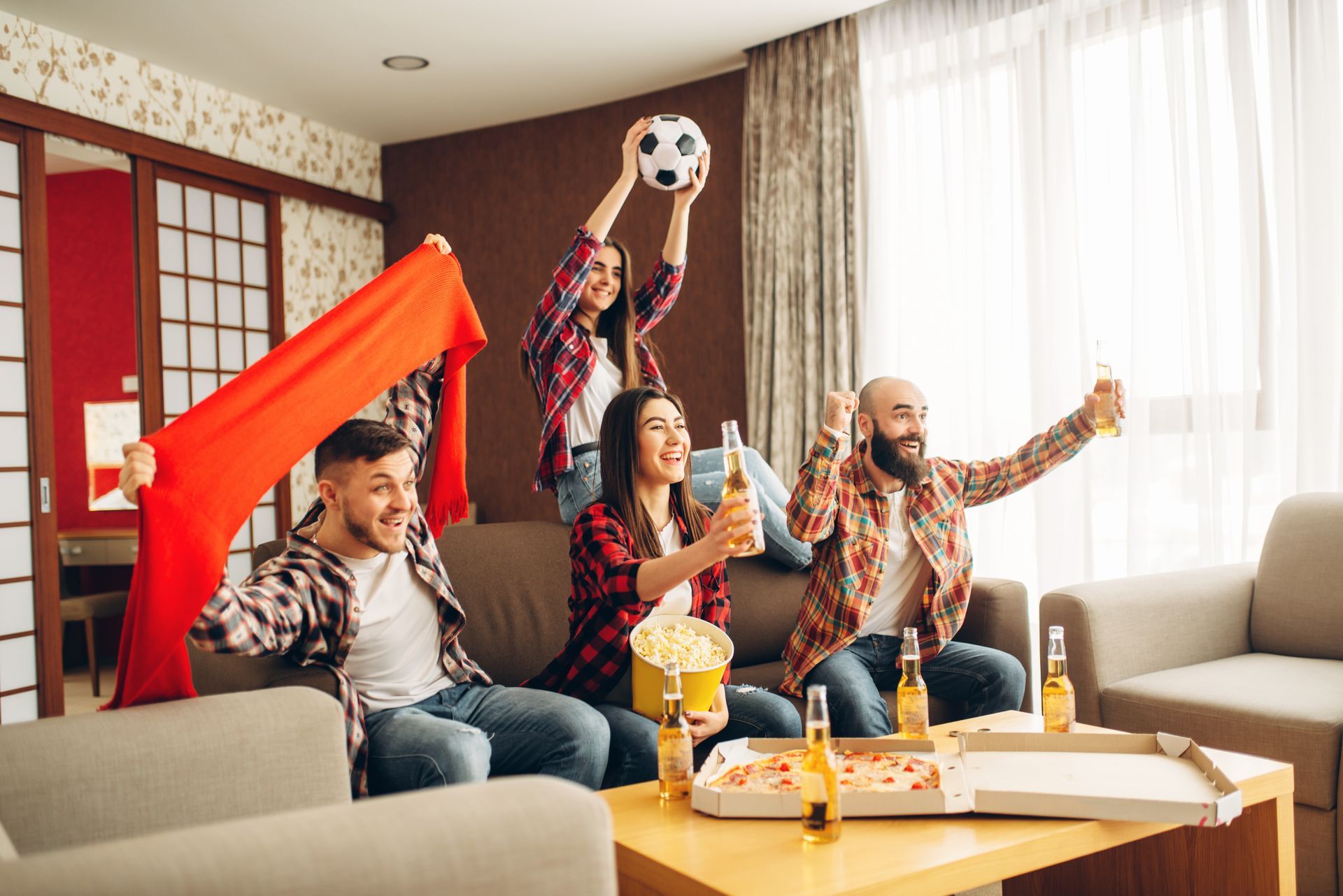 Un gruppo di amici festeggia una partita di calcio in un salotto con birra, pizza, popcorn e una bandiera.