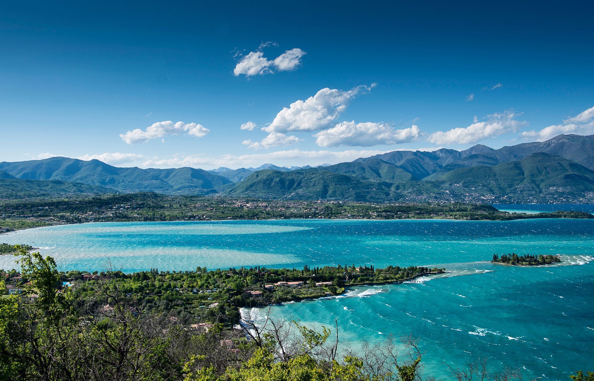 Bright turquoise lake with rolling hills, mountains, and a blue sky with fluffy clouds.