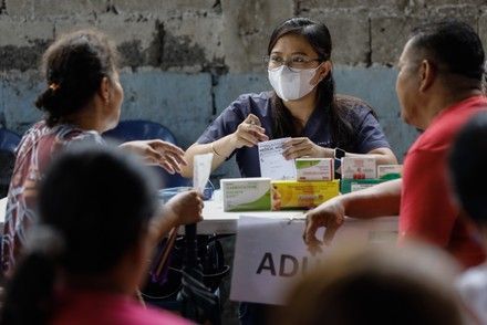 A medical worker in a mask assisting two people, medicines on a table in a community setting.