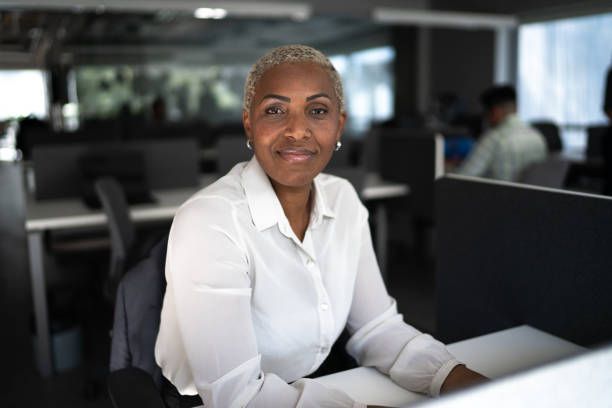 Smiling Black woman with short silver hair in a white shirt at an office desk.