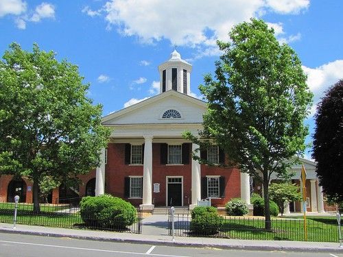 Brick building with white columns, topped with a cupola, trees and blue sky.