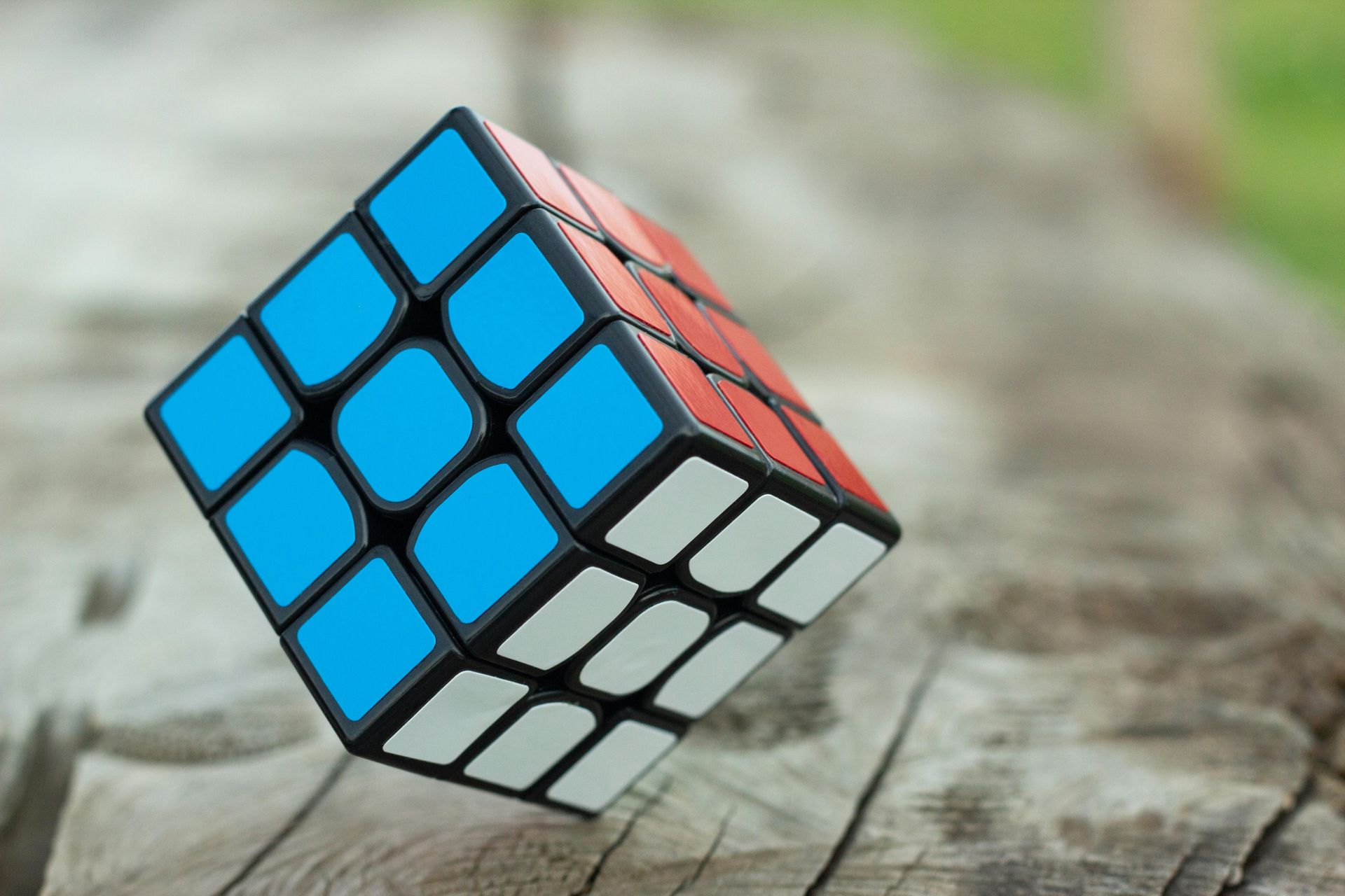 Rubik's Cube with blue, red, and white faces balanced on a wooden surface.