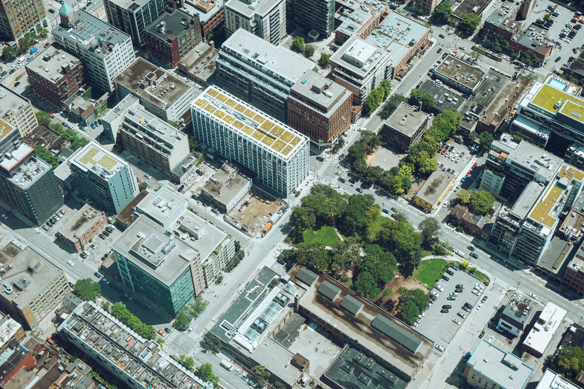 Aerial view of a city block with buildings, roads, and a small park with trees.