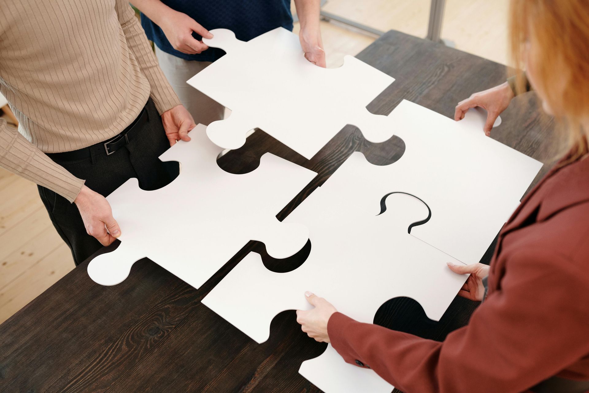 People assembling a giant jigsaw puzzle on a dark table, collaborative effort.