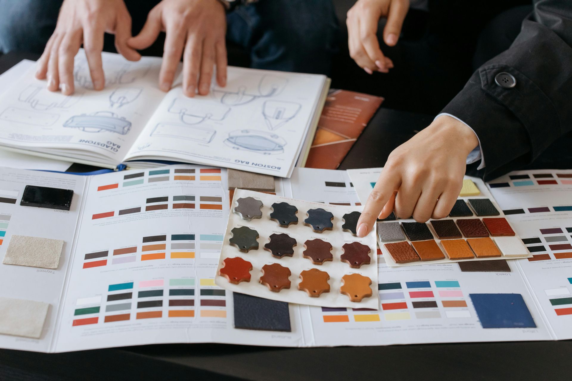 Hands pointing at leather swatches and color palettes, discussing design ideas.