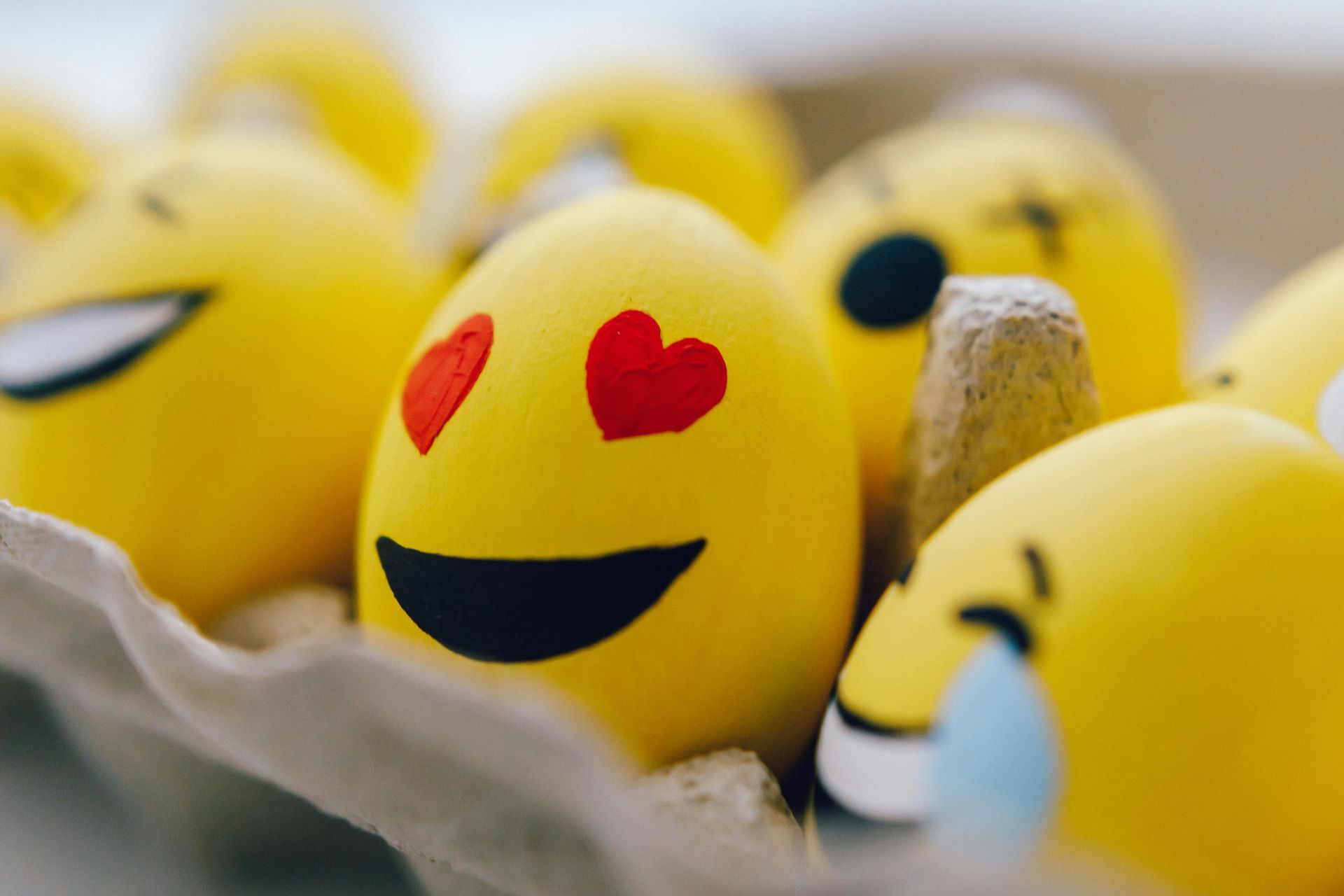 Yellow Easter eggs decorated with emoji faces in a carton; one has heart eyes.