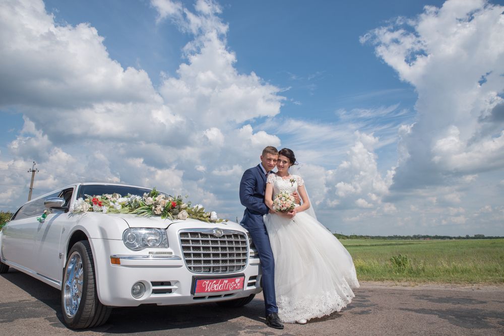 A bride and groom are posing for a picture in front of a white limousine.