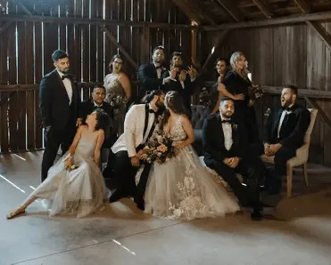 A large wedding party is posing for a picture in a barn.