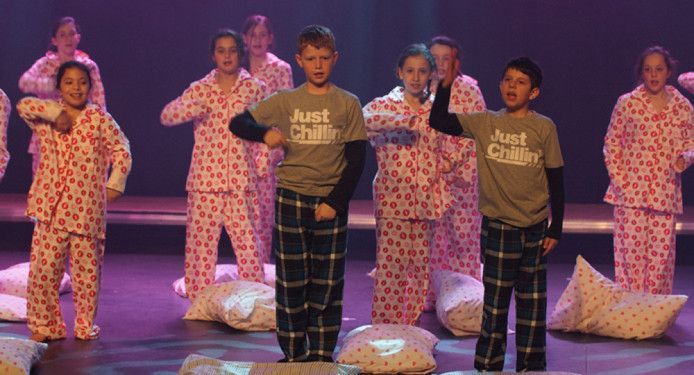 A group of children wearing pajamas are dancing on a stage.