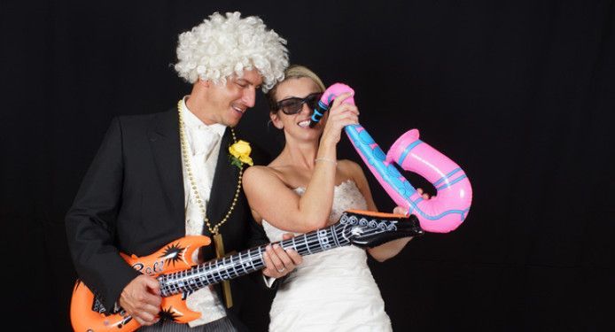 A bride and groom are posing for a picture with a guitar and balloons.