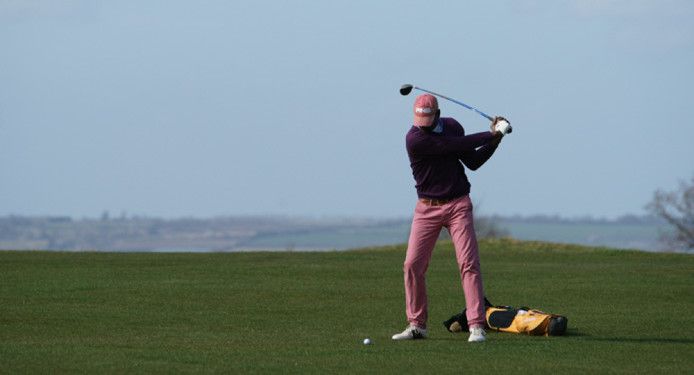 A man is swinging a golf club on a golf course.