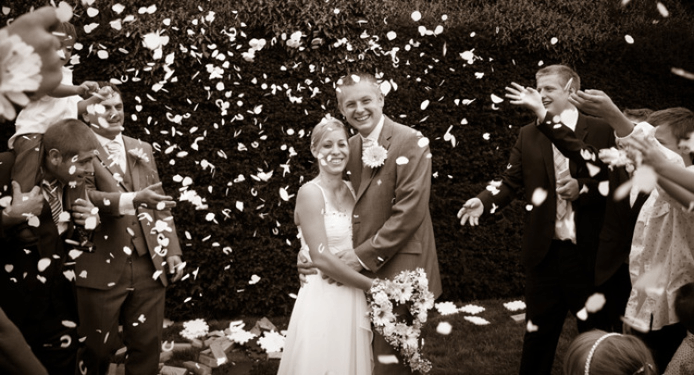 A bride and groom are standing in front of a crowd of people throwing confetti.