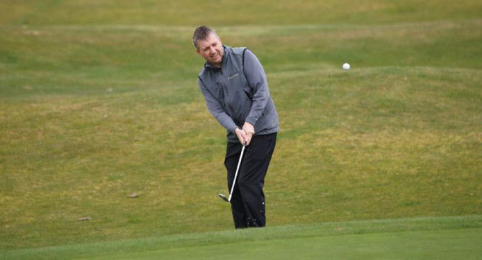 A man is hitting a golf ball out of a bunker on a golf course.