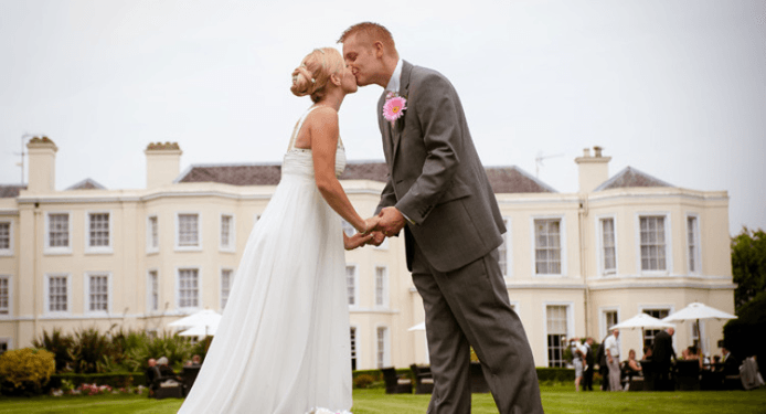 A bride and groom are kissing in front of a large building.