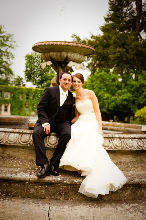 A bride and groom are posing for a picture in front of a fountain.
