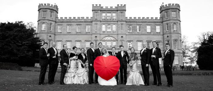 A group of people standing in front of a castle holding a red heart umbrella.