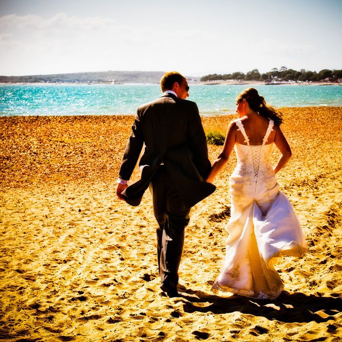 A bride and groom are walking on the beach holding hands