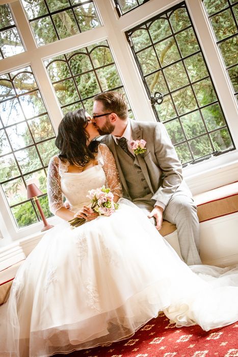 A bride and groom are kissing in front of a window.