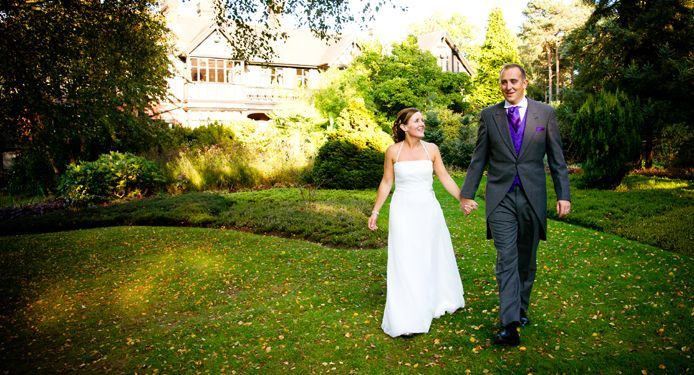 A bride and groom are walking through a grassy field holding hands.