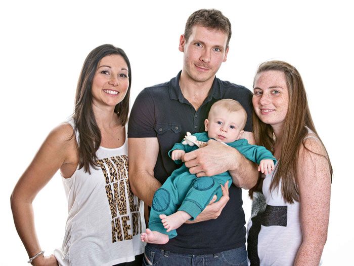 A man is holding a baby while two women stand behind him