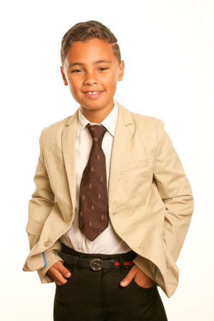 A young boy wearing a suit and tie with his hands in his pockets
