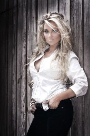 A woman in a white shirt and black jeans is standing in front of a wooden wall.