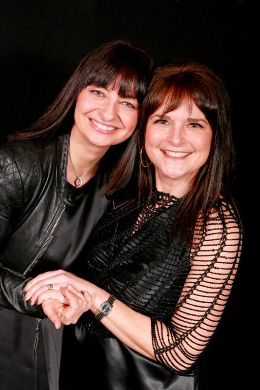 Two women are standing next to each other holding hands and smiling.