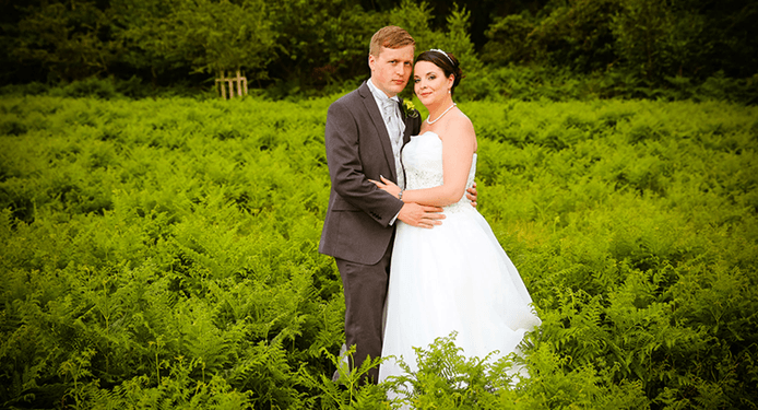 A bride and groom are posing for a picture in a field of ferns.