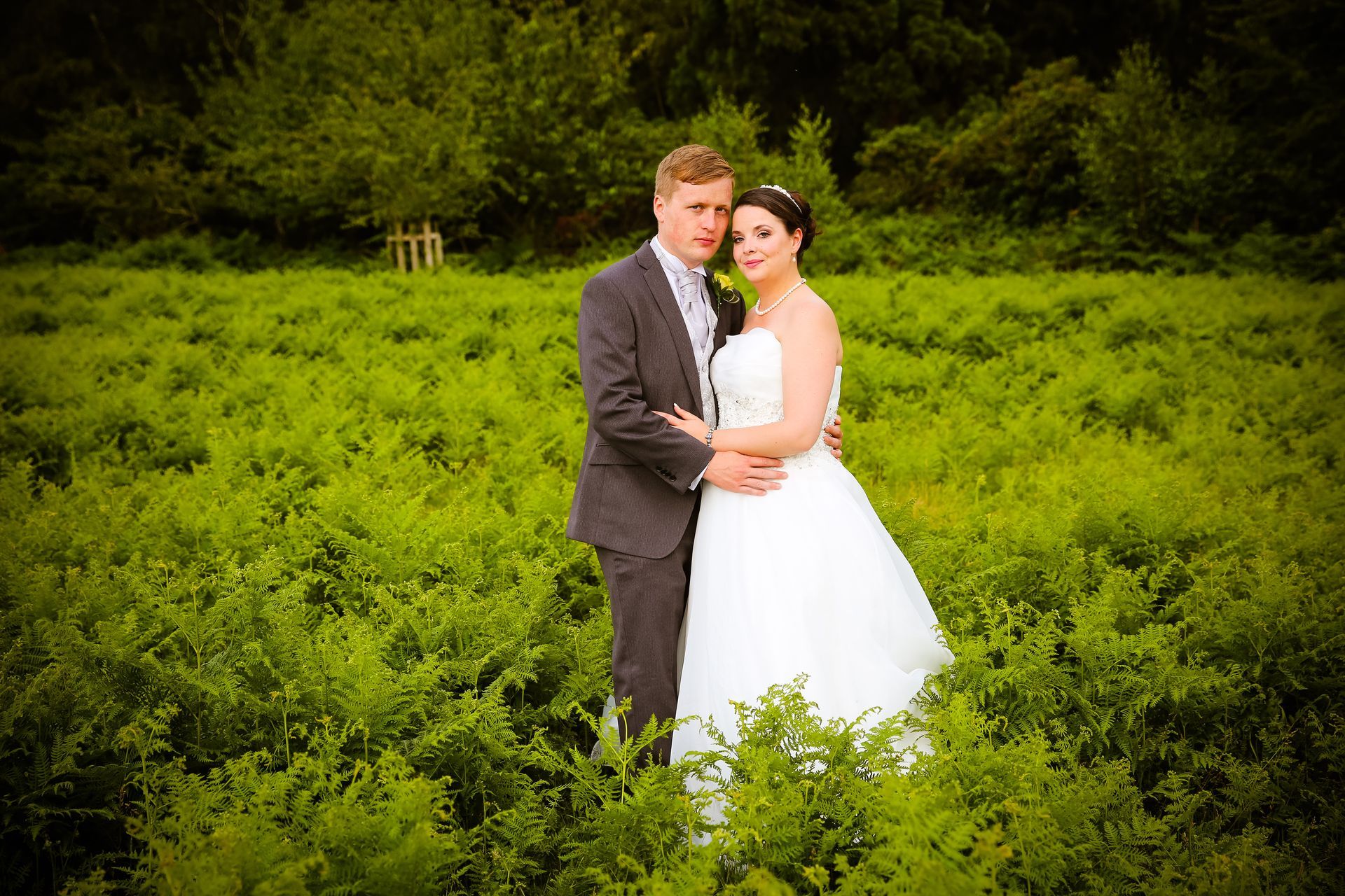 A bride and groom are posing for a picture in a field of ferns.