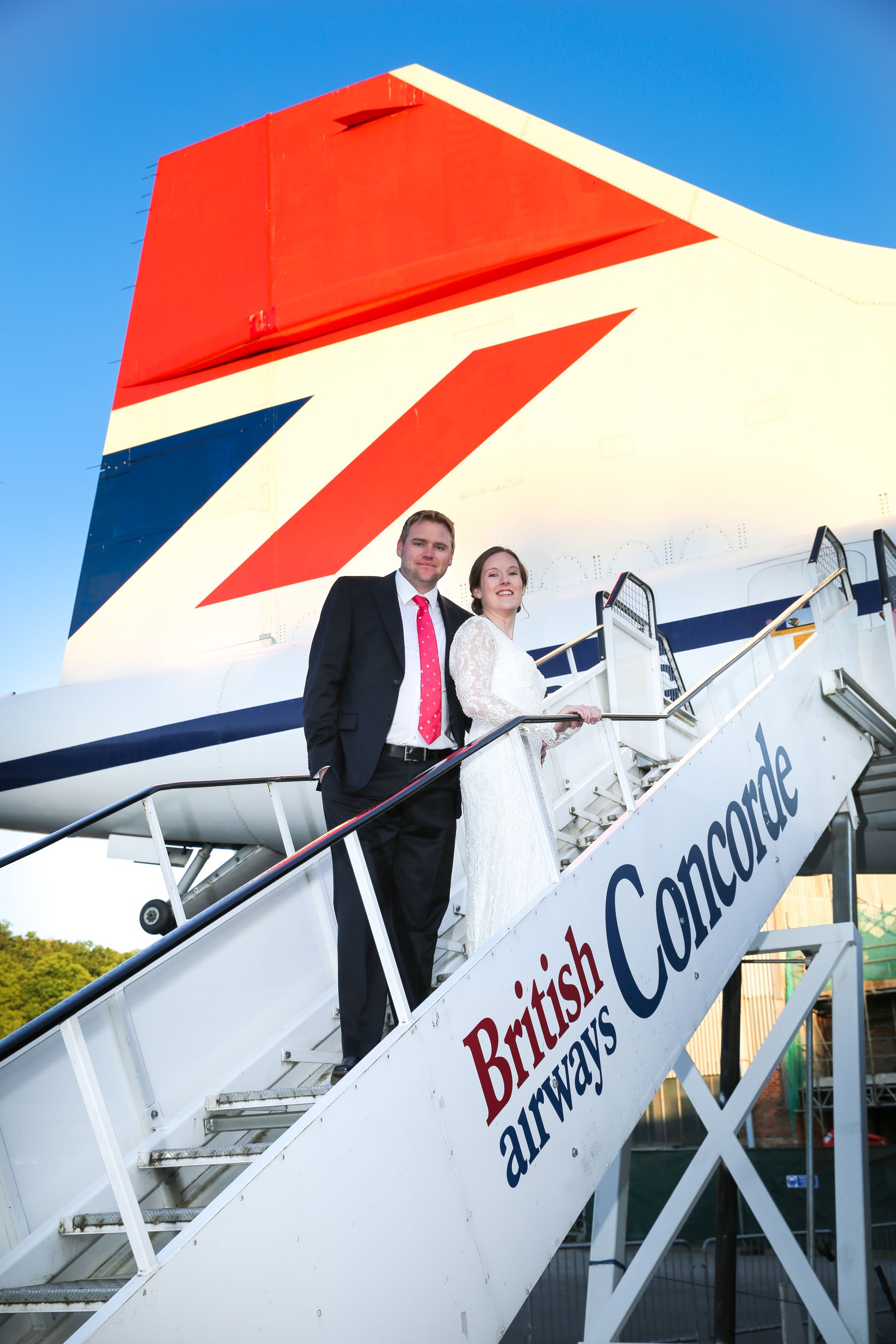 A bride and groom are standing on the stairs of a british airways plane