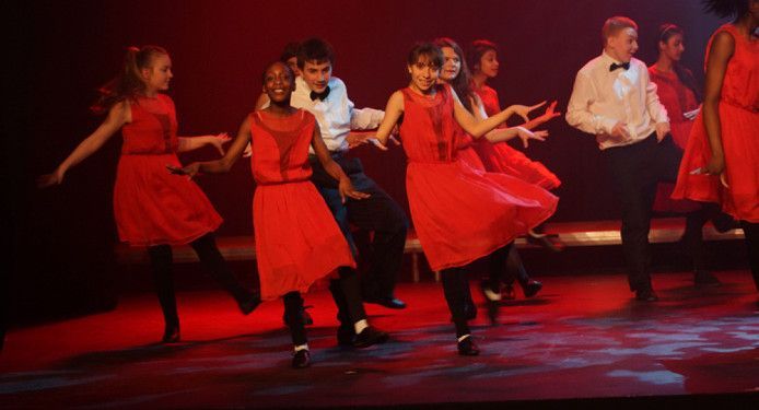 A group of people in red dresses are dancing on a stage.