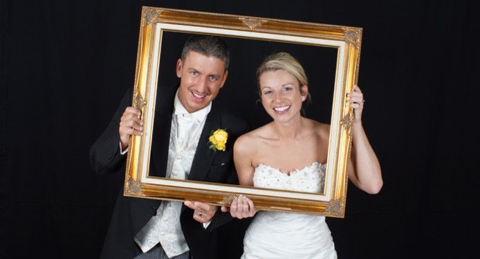 A bride and groom are holding a picture frame.