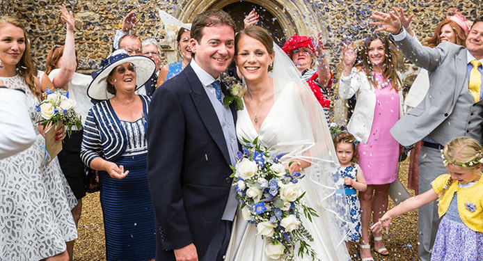 A bride and groom are standing in front of a church surrounded by their wedding guests.